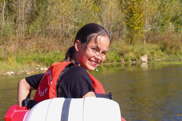 Ein junges Mädchen sitzt im Kanu und dreht sich lächelnd zur Kamera um