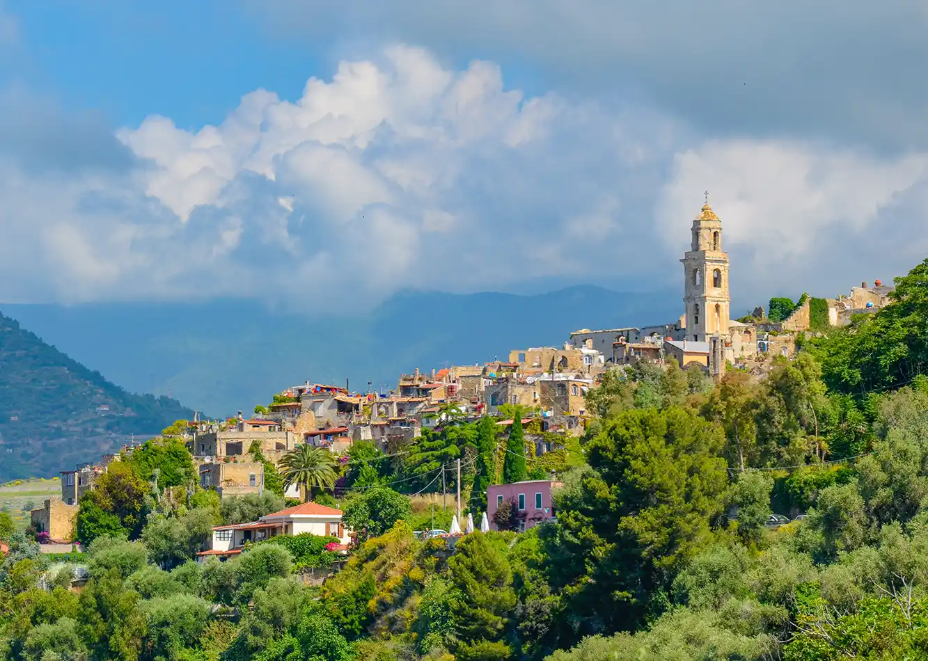 Altes Dorf mit Ruinen und Kirchturm inmitten hügeliger Landschaft bei bewölktem Himmel