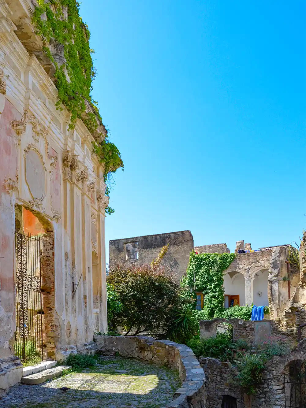 Links Ruine einer Kirche, dahinter Mauerreste und ein blaues Handtuch über einer Mauer