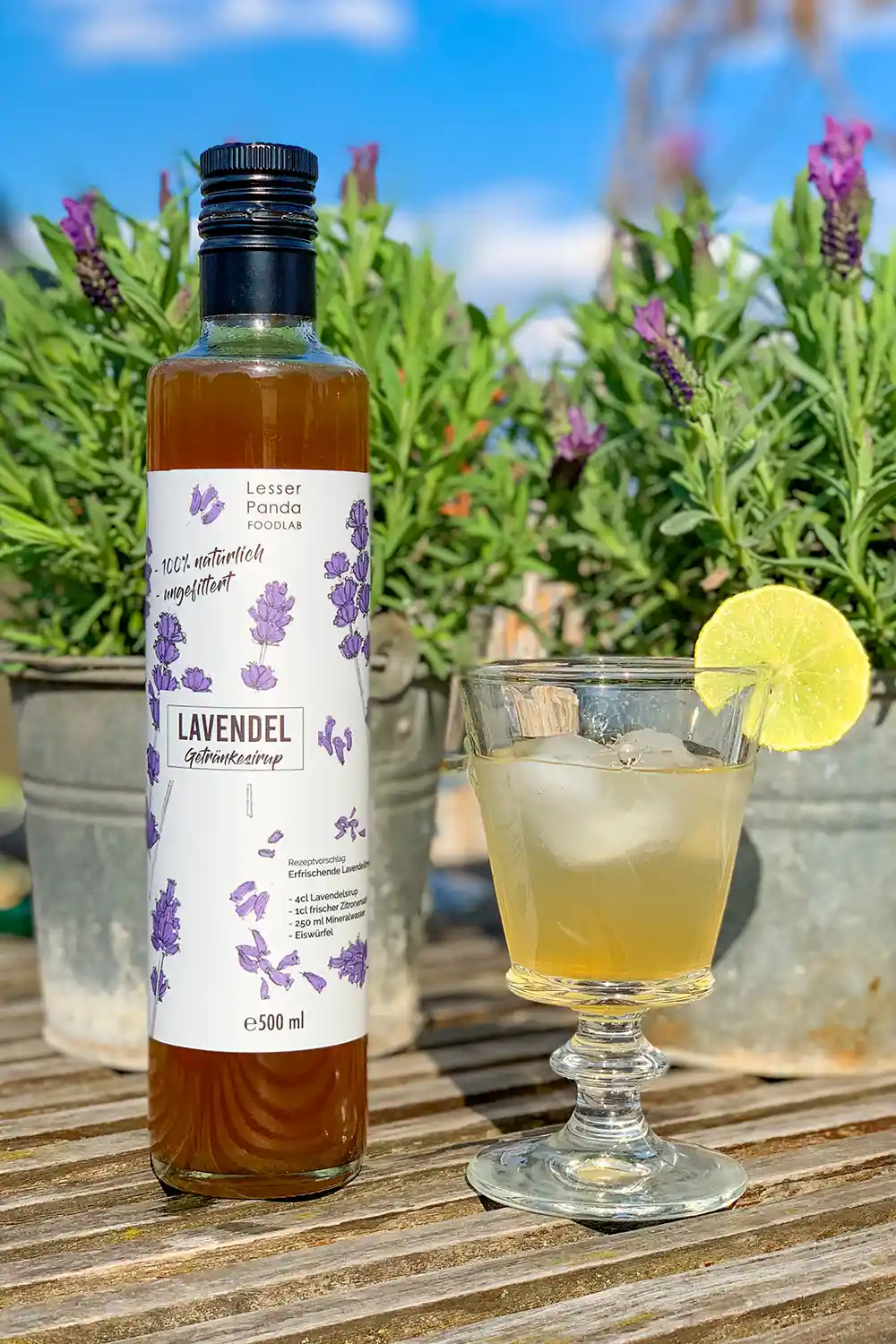 Alkoholfreier-Sommerdrink-Lavendel Flasche Lavendelsirup und Glas vor Lavendelsträuchern