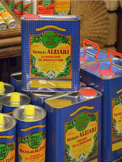 Bunte Dosen mit Olivenöl von Nicolas Alziari stapeln sich dicht an dicht in einem Ladenregal.