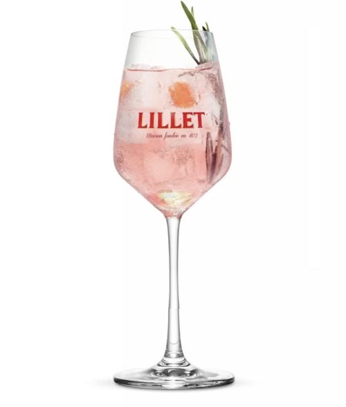 Ein Glas rosa Cocktail mit Eis, garniert mit Kräutern und dem Lillet-Logo auf dem Glas.