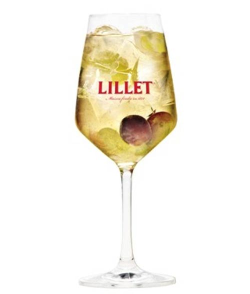 Ein Weinglas mit Lillet-Logo, gefüllt mit einem leichten Getränk, Eis und garniert mit Weintrauben und Kräutern.