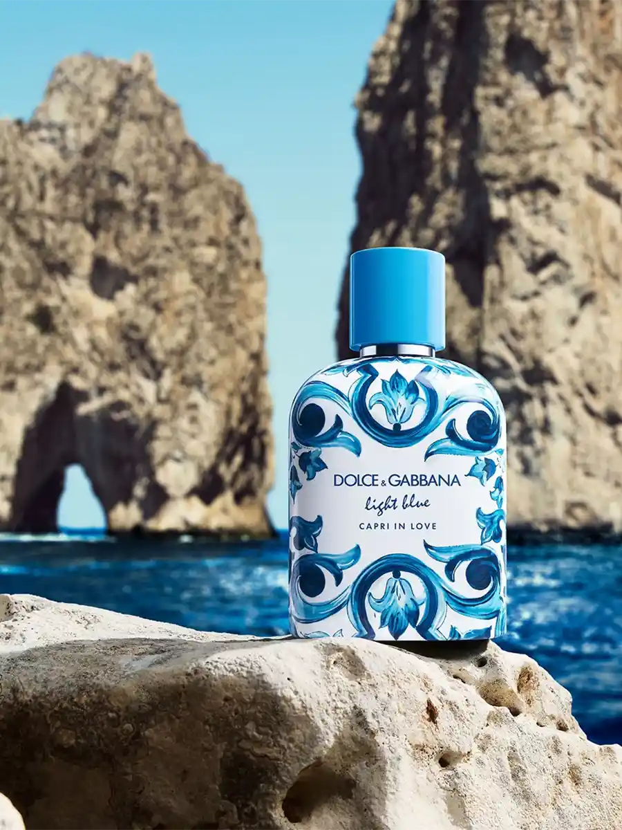 Blauweiße Parfümflasche auf einem Felsen am Meer, mit Klippen und blauem Himmel im Hintergrund.