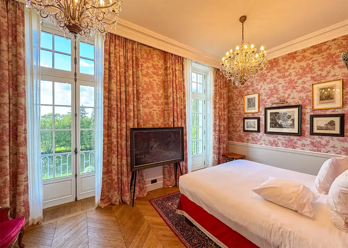 Elegantes Schlafzimmer mit Tapete und Gardinen in Toile de Jouy, großem Bett, Kronleuchtern und hohen Fenstern mit Blick ins Grüne.