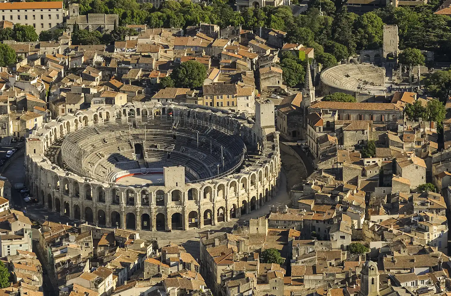 Luftaufnahme eines römischen Amphitheaters, umgeben von historischen Gebäuden und engen Straßen.