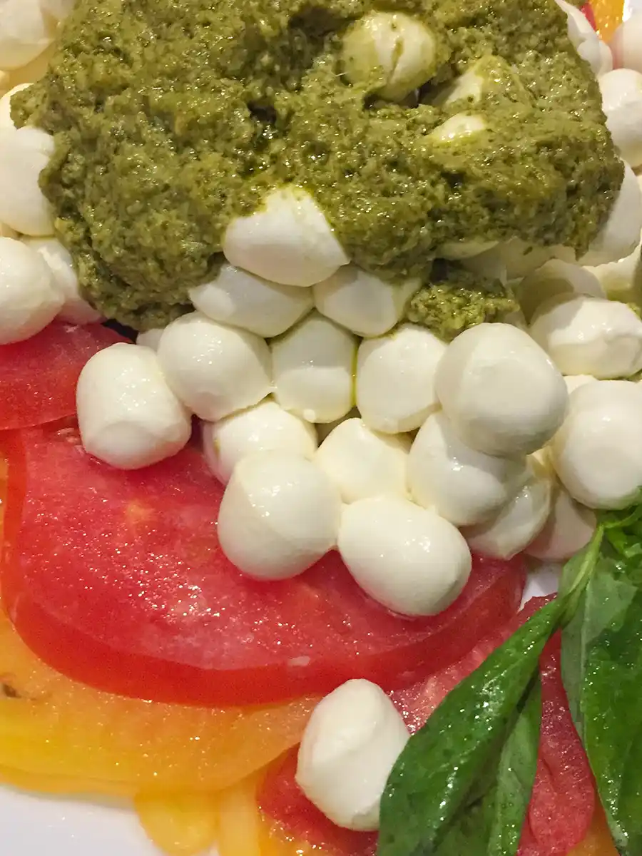 Mini-Mozzarella-Pesto In Scheiben geschnittene Tomaten, belegt mit Mozzarellakugeln, Pestosauce und frischen Basilikumblättern.