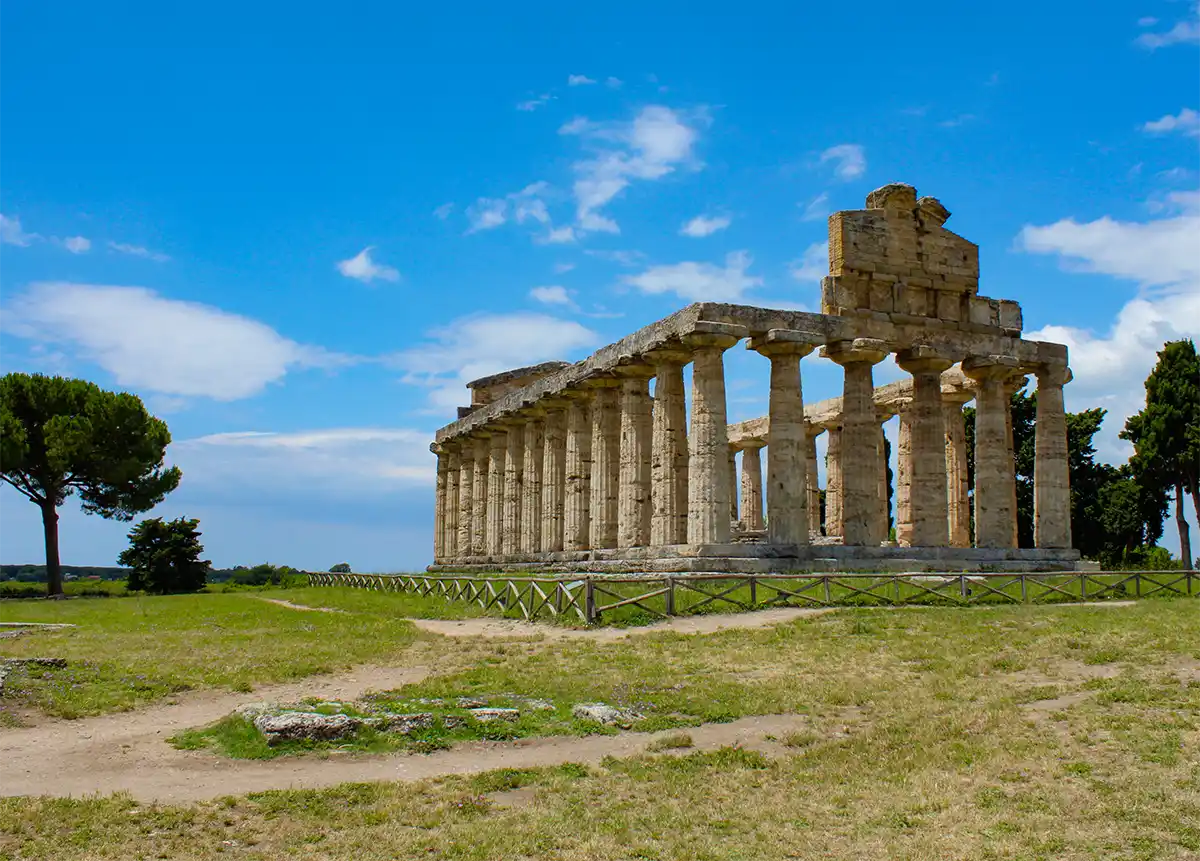 Tempel-Paestum Antike griechische Tempelruinen mit Steinsäulen unter blauem Himmel, umgeben von Gras und Bäumen.