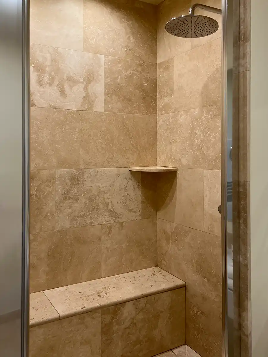 Badezimmer-mediterran-Dusche-Travertin Dusche mit hellbraunen Steinfliesen, eingebauter Bank, Eckregal und Regendusche.