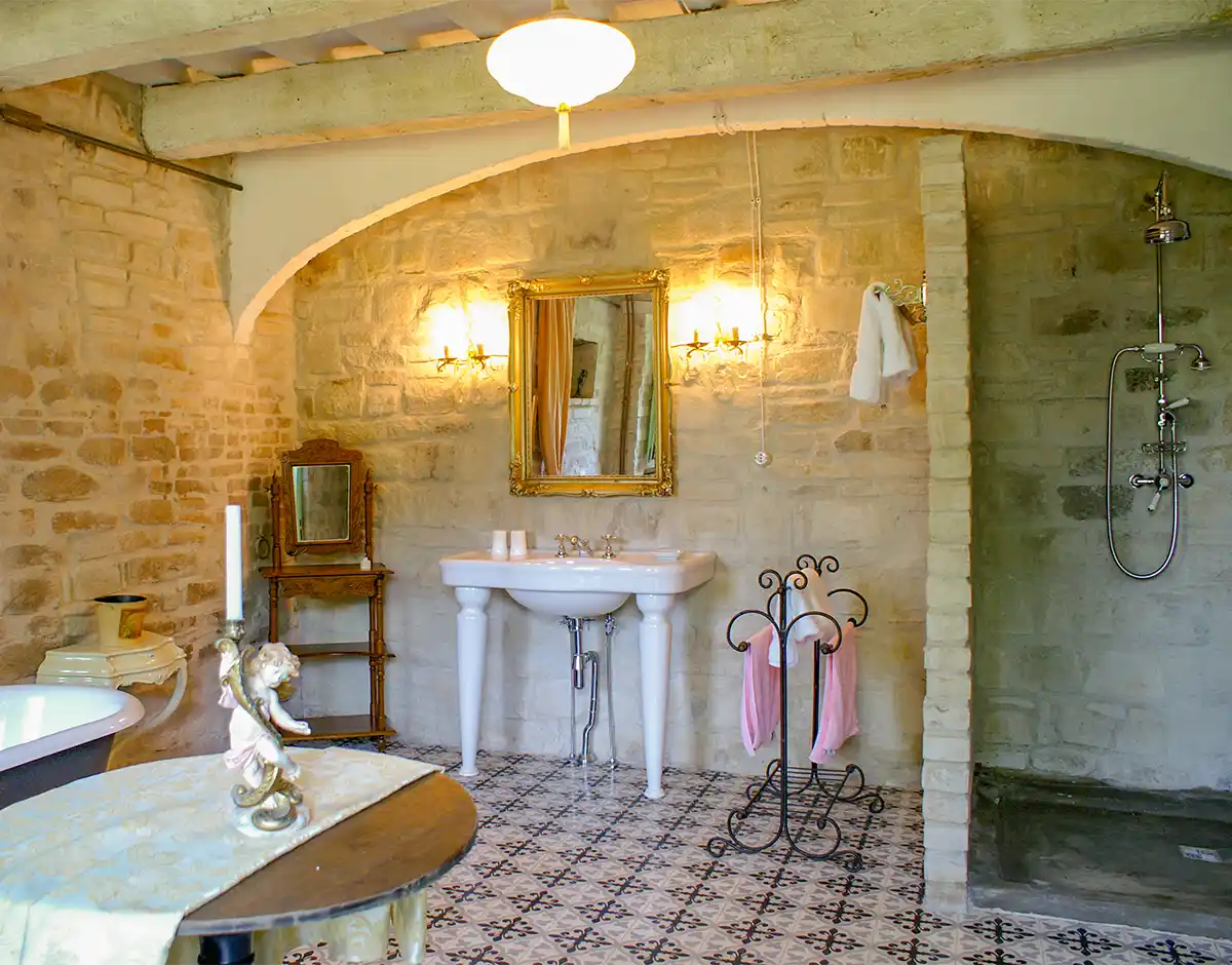 Badezimmer-mediterran-Italien-Bauernhof-2 Rustikales Badezimmer mit Steinwänden, Sockelwaschbecken, goldgerahmtem Spiegel und offenem Duschbereich.