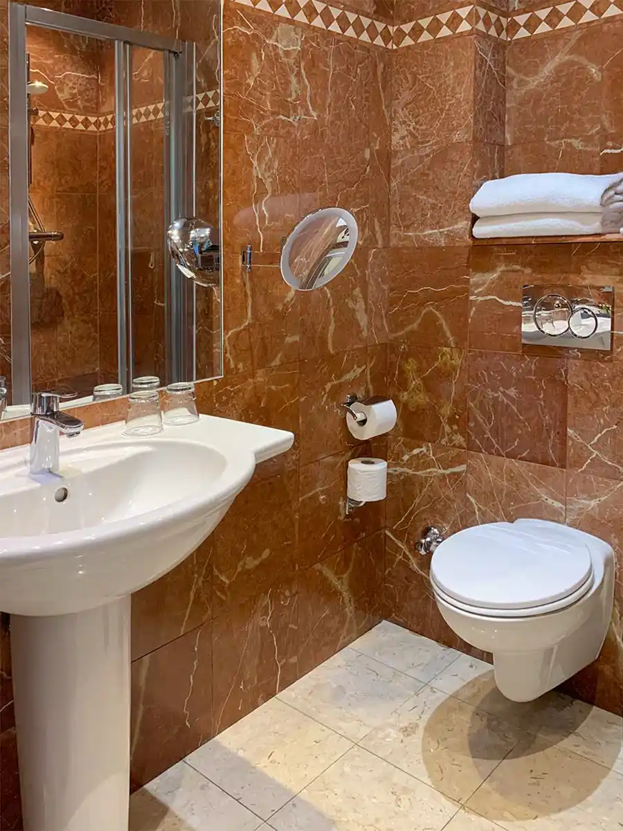 Badezimmer-mediterran-Nizza Modernes Badezimmer mit roten Marmorwänden, weißem Waschbecken, wandmontierter Toilette, Handtüchern und großem Spiegel.