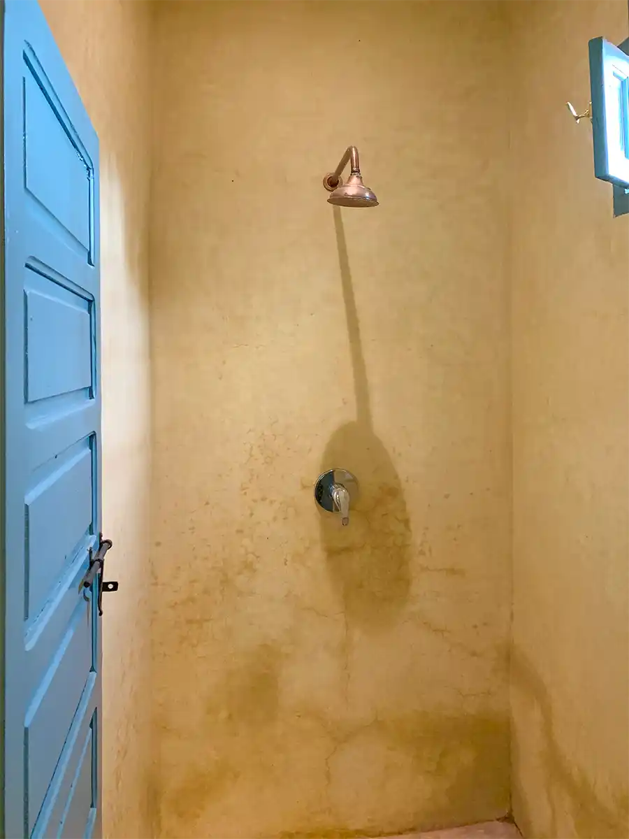 Badezimmer-mediterran-Tadelakt-Marrakesch Kleiner, schlichter Duschraum mit hellbraunen Wänden, einer blauen Tür und einem einzigen Duschkopf unter einem kleinen Fenster.