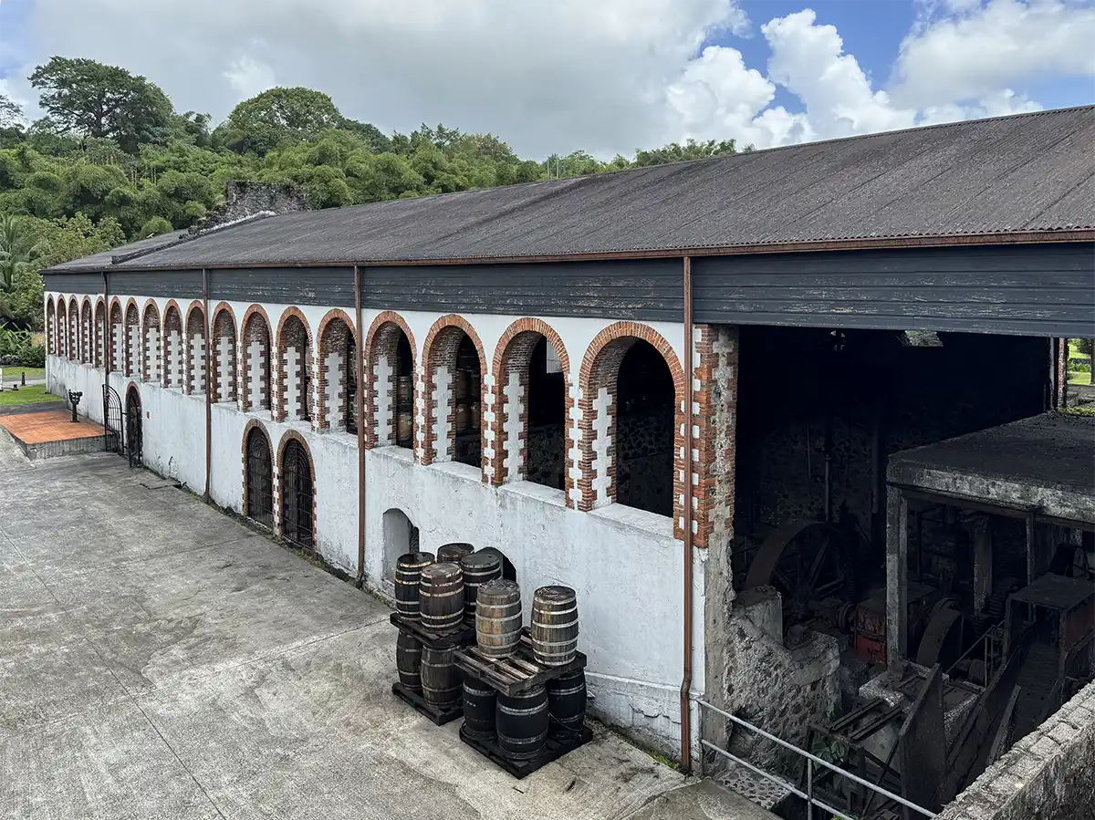 Habitation-HSE Großes altes weißes Gebäude mit gewölbten Fenstern, draußen gestapelten Fässern und üppigem Grün im Hintergrund.
