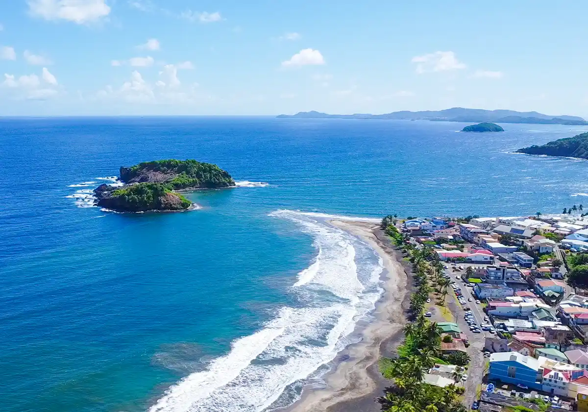Martinique-Inseln-Sainte-Marie Luftaufnahme einer Küstenstadt mit blauen Meereswellen, Sandstrand und kleinen grünen Inseln vor der Küste.