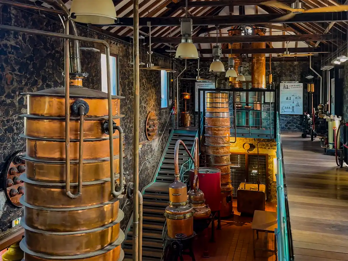 Martinique-Rum-Destillation-Museum Kupferne Säulen aus übereinandergeschichteten Böden sowie kupferne Brennblasen im Museum aus grauem Stein und Holzbalken