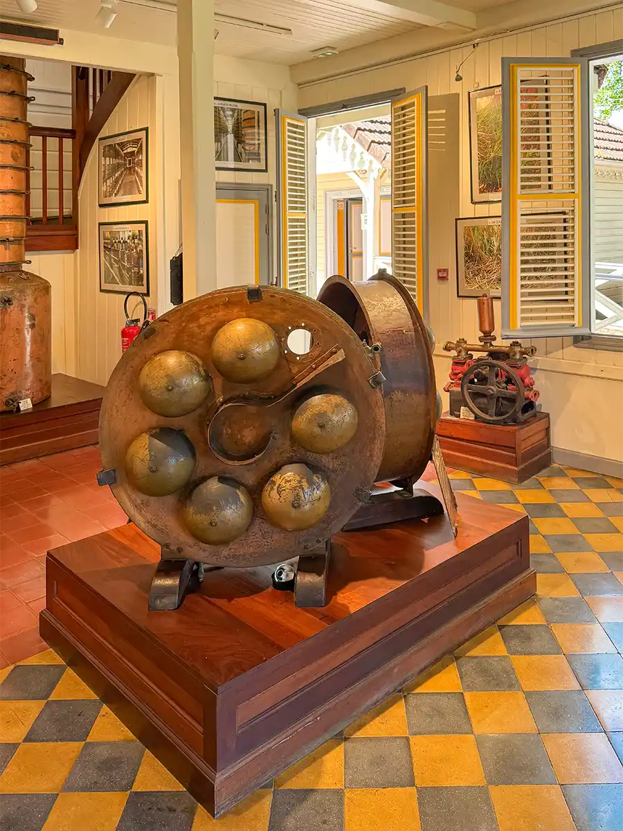 Martinique-Rum-Tablet-Kolonne Großer antiker Destillationsapparat aus Metall, ausgestellt in einem Museumsraum mit gelb-grauem Schachbrettboden.