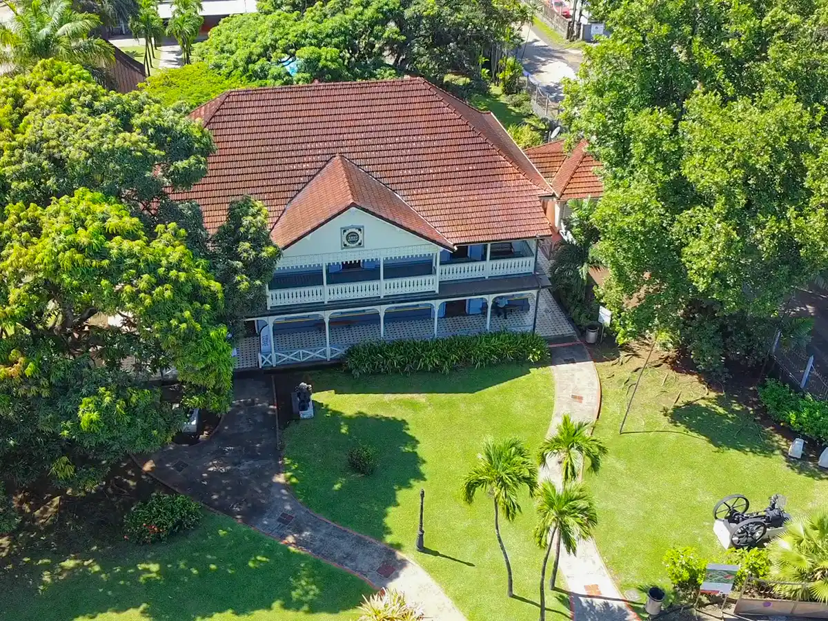 Rum-Museum-Saint-James-Haus-von-oben Luftaufnahme eines Hauses mit rotem Dach, breiter Veranda und Garten, umgeben von Bäumen und einem geschwungenen Weg.
