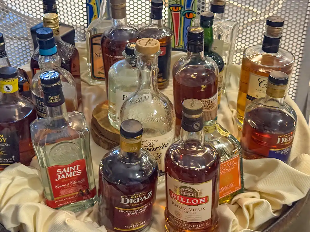 Rumsorten-Martinique Verschiedene Rumflaschen, die auf einem mit Stoff bedecktem Fass dicht nebeneinander ausgestellt sind.