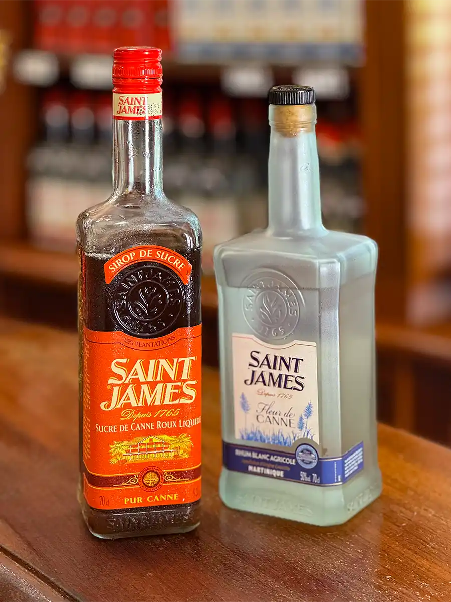 Weisser-Rum-Zuckerrohrsirup Zwei Flaschen Saint-James-Rum auf einer Holztheke, eine klar und eine bernsteinfarben.