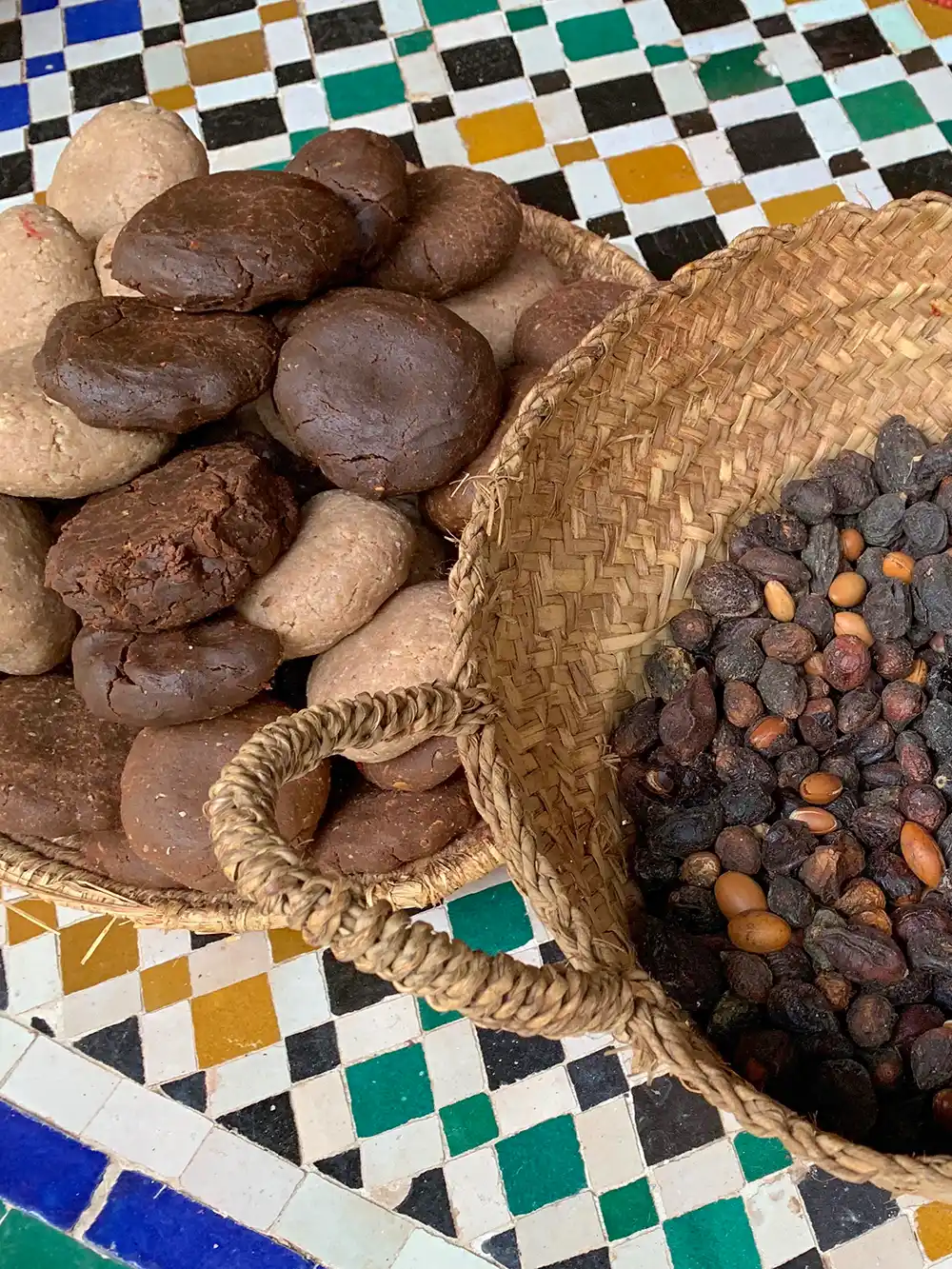 Zwei geflochtene Körbe: einer enthält braune und beigefarbene Scheiben, der andere kleine dunkelbraune Samen, die auf bunten Fliesen liegen.