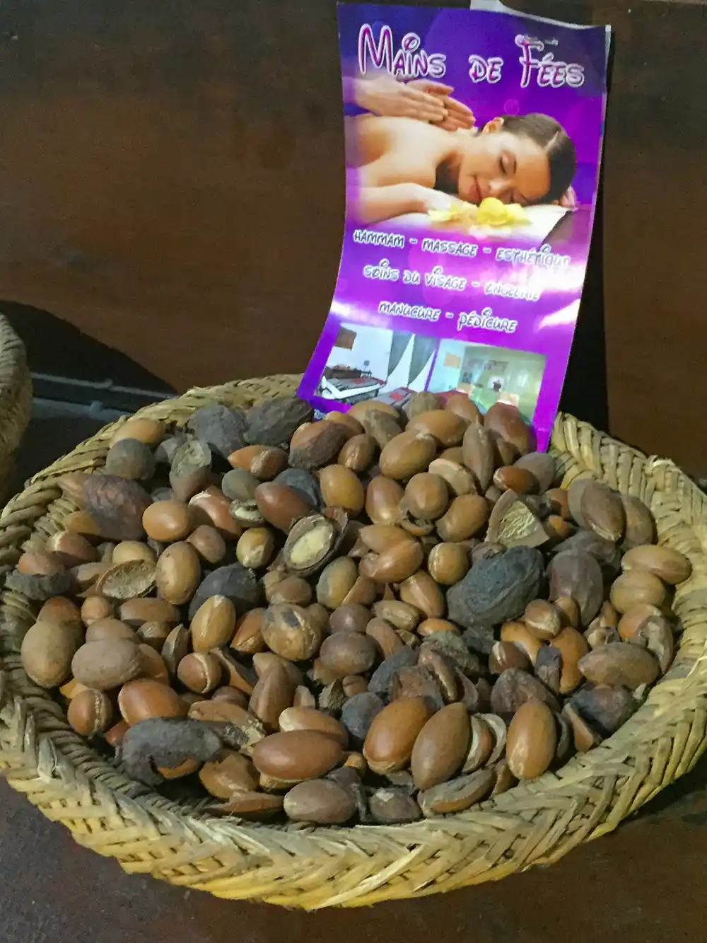Ein geflochtener Korb, gefüllt mit Argan-Nüssen, im Hintergrund ein Flyer mit Wellness-Angeboten.