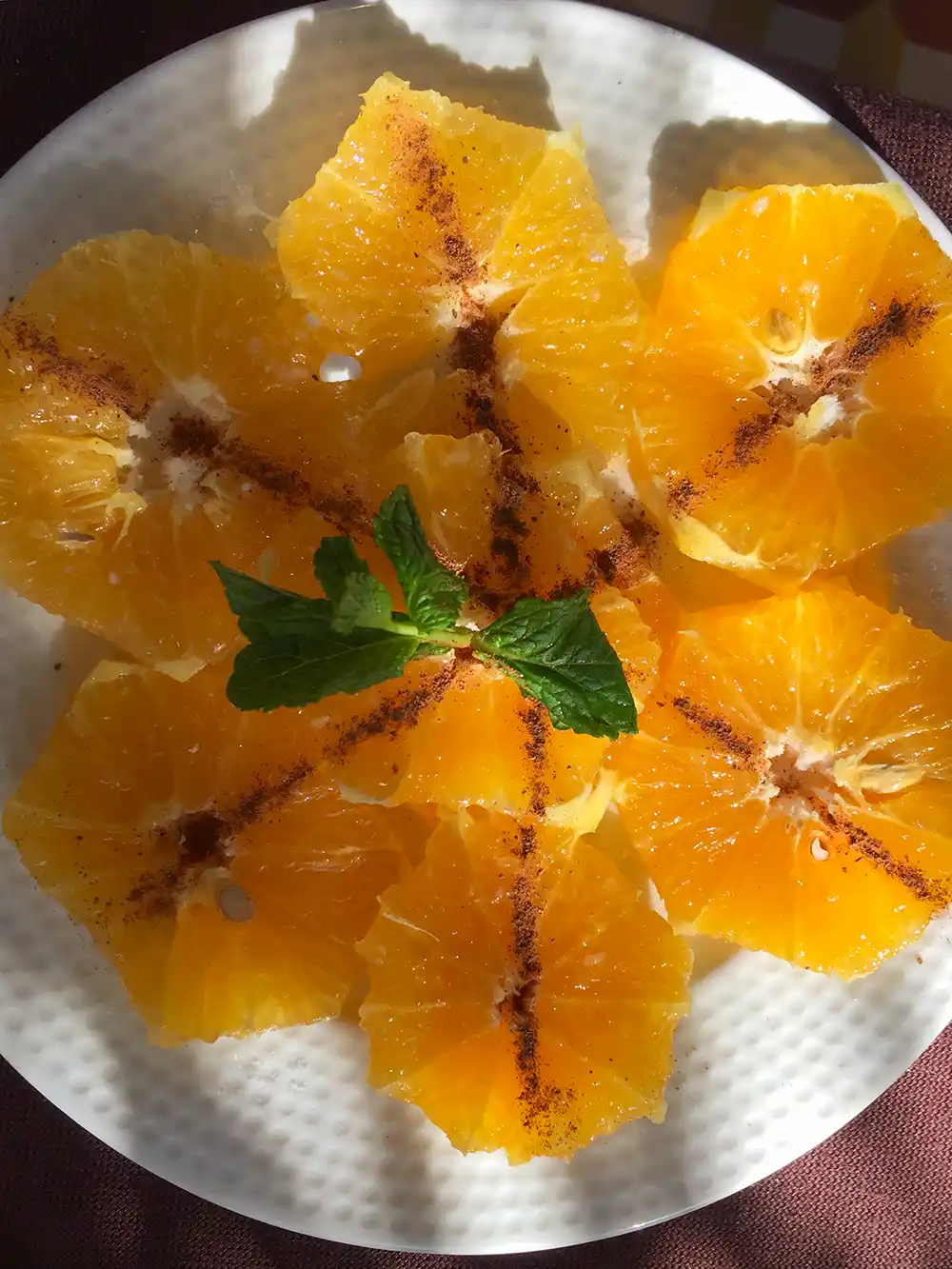 Ein Teller mit kreisförmig angeordneten Orangenscheiben, die mit Minzblättern belegt und mit Chilipulver bestreut sind.