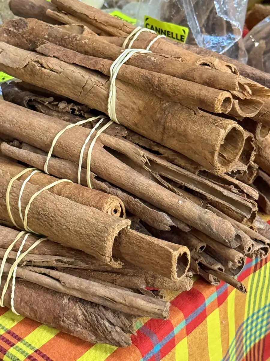 Martinique-Marche-Zimt Mit Schnur gebundene Zimtstangenbündel, die auf einem bunt karierten Tuch auf einem Markt gestapelt sind.