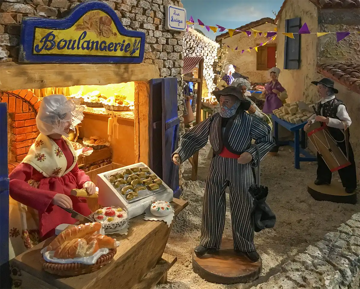 Santons-Boulangerie-Aubagne-Weihnachtsmarkt Diorama einer französischen Bäckereiszene mit Figuren, Brot, Gebäck und Steingebäuden in einer Dorfstraße.