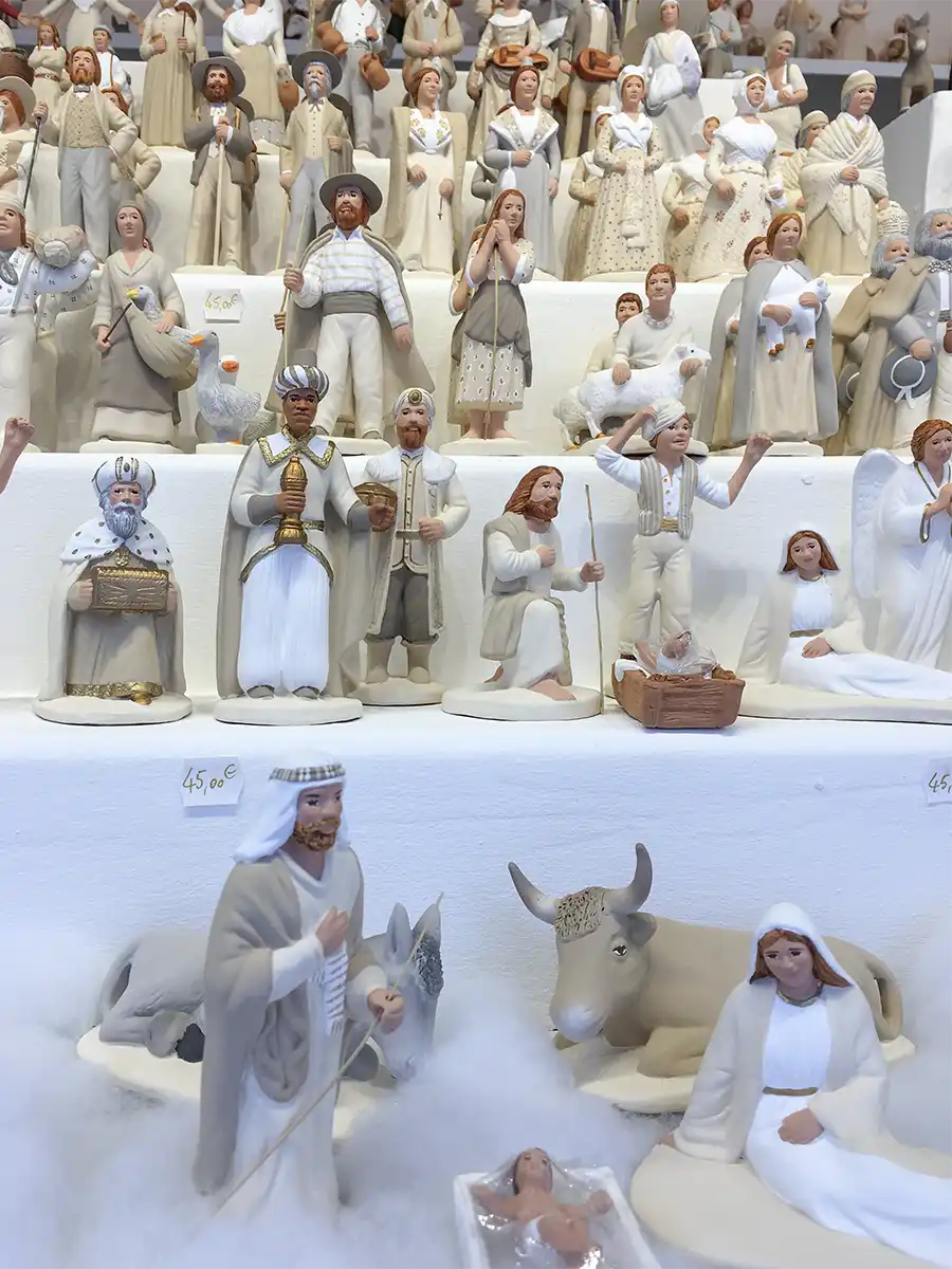 Santons-Marseille-Weihnachtsmarkt Auf weißen Regalen stehen handgefertigte Krippenfiguren, die Menschen, Tiere und Engel darstellen.