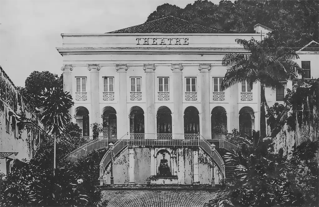 Sehenswuerdigkeiten-Martinique-Theater-Saint-Pierre Historisches weißes Theatergebäude im Kolonialstil mit Bogenfenstern, Treppenhaus und tropischen Pflanzen.