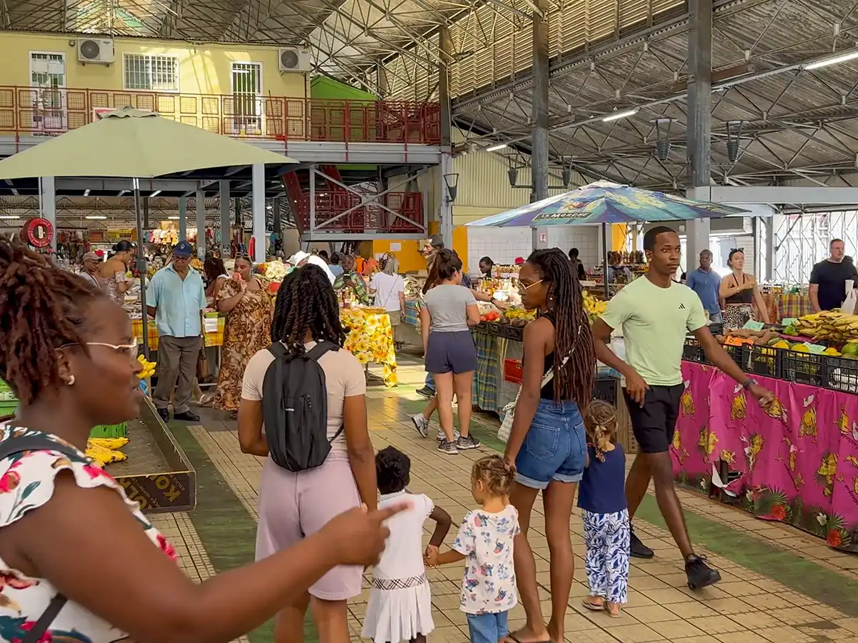 Sehenswurdigkeiten-Martinique-Markthalle Belebte Markthalle mit Erwachsenen und Kindern, die unter einem hohen Dach zwischen bunten Verkaufsständen spazieren gehen.