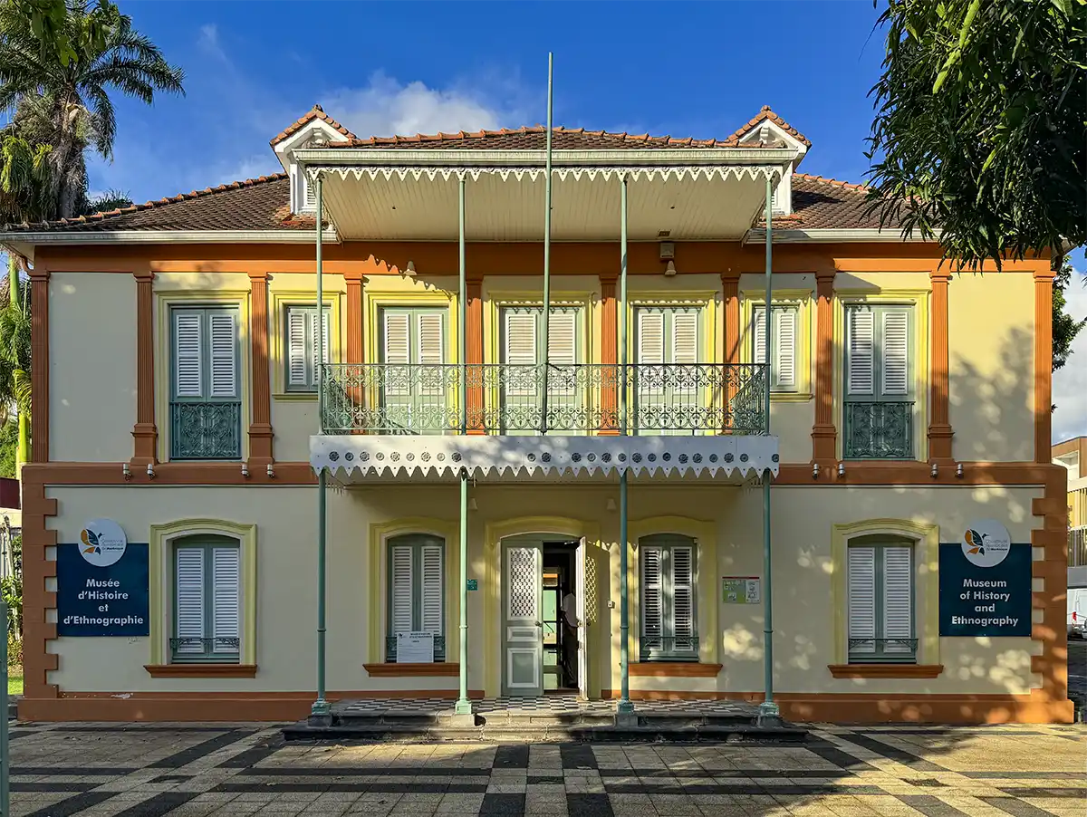 Sehenswurdigkeiten-Martinique-Museum Zweistöckiges gelb-weißes Museumsgebäude mit Fensterläden, Balkon und einer zentralen offenen Tür.
