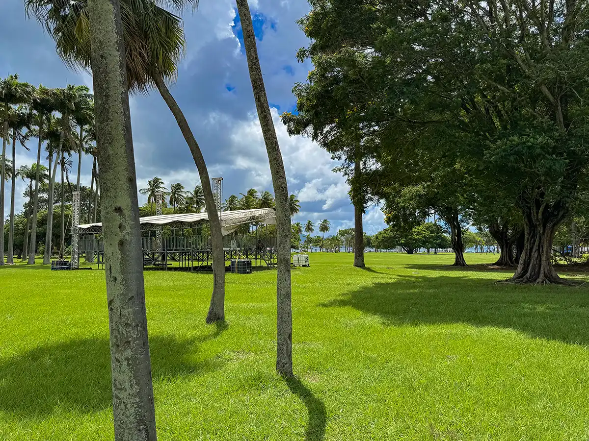 Sehenswurdigkeiten-Martinique-Park-la-Savane Außenbühne auf einer Wiese mit Palmen und großen Laubbäumen unter einem teilweise bewölkten Himmel.