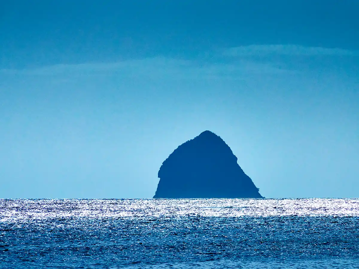 Straende-Martinique-Diamant-Insel Eine einsame Felseninsel erhebt sich aus dem glitzernden blauen Meer unter einem klaren Himmel.