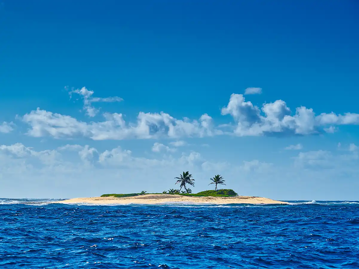 Straende-Martinique-Insel Eine kleine Sandinsel mit Palmen, umgeben von blauem Meer unter einem hellen Himmel mit vereinzelten Wolken.