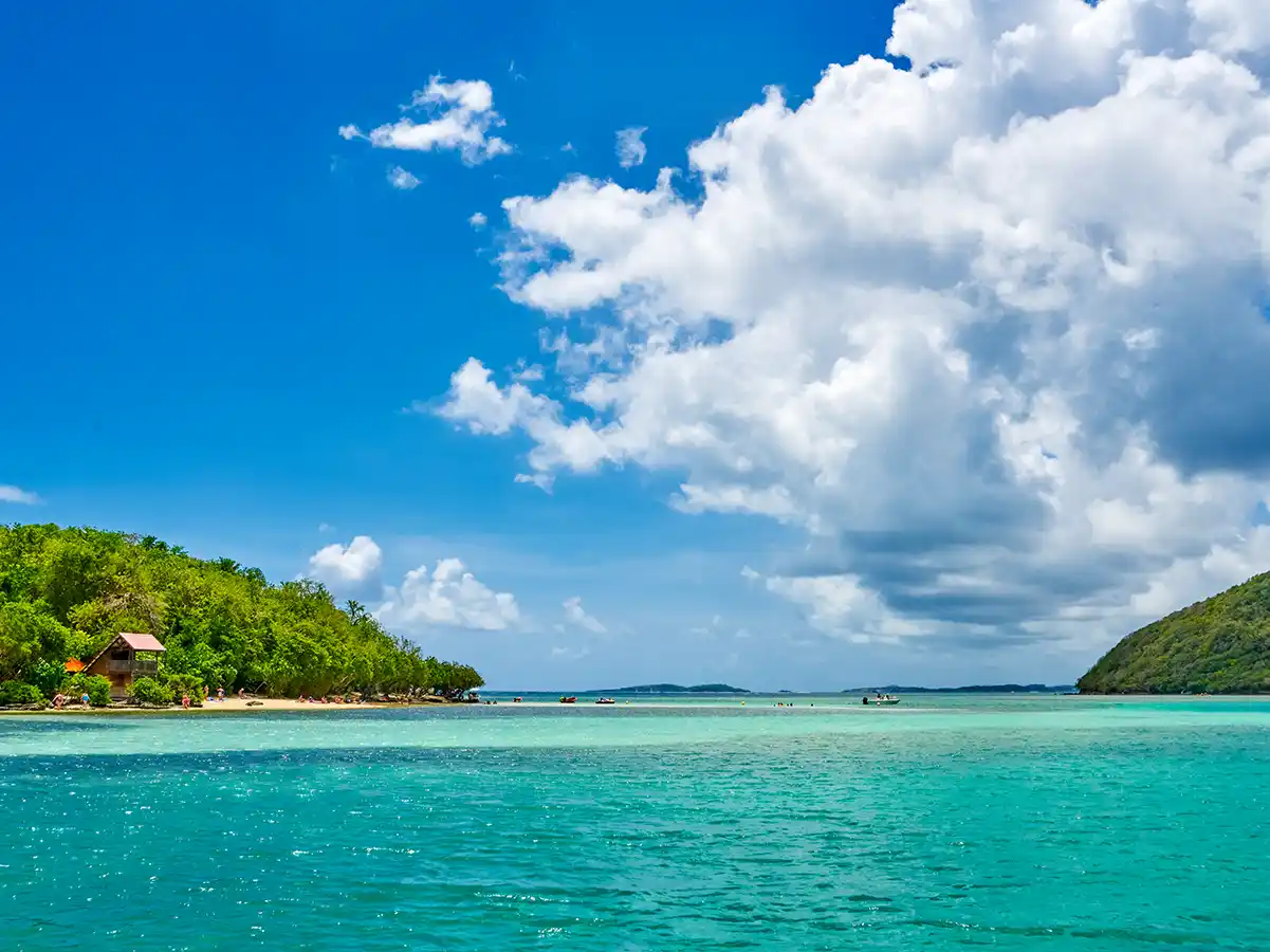 Straende-Martinique Türkisfarbenes Meerwasser, grüne Inseln und ein teilweise bewölkter blauer Himmel mit einer kleinen Hütte in Ufernähe.