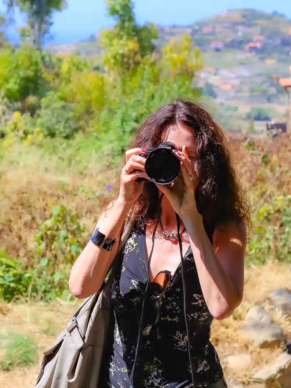Frau mit lockigem Haar, die ein Foto im Freien an einem sonnigen Tag macht, mit einer unscharfen Landschaft im Hintergrund.