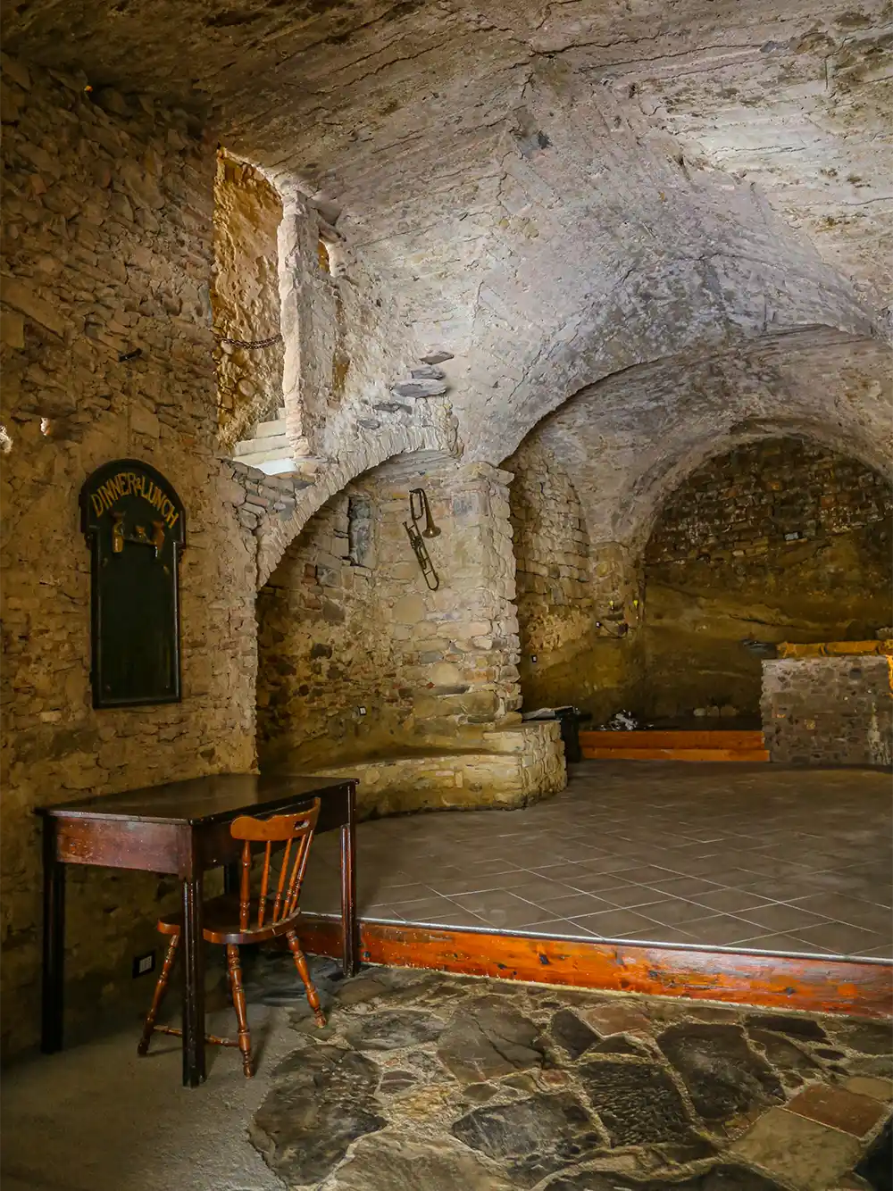 Ein rustikaler Raum mit Steinmauern, gewölbten Decken, einem Holztisch und einem einzigen Stuhl.