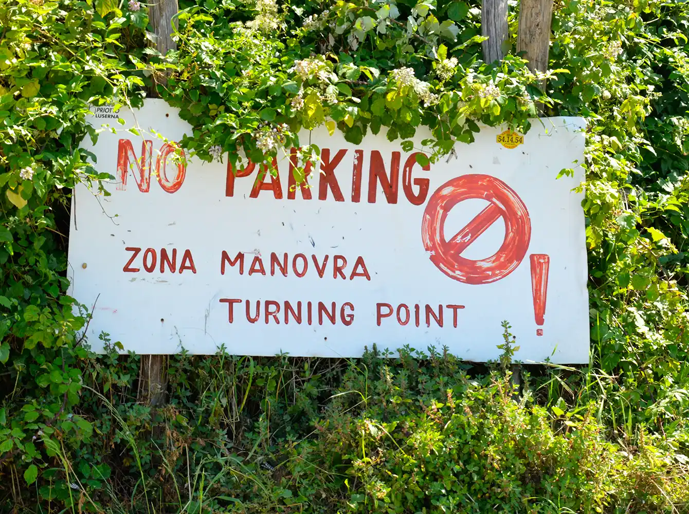Ein Schild mit der Aufschrift Parkverbot, Zona Manovra, Wendepunkt, umgeben von grünen Büschen und Pflanzen.