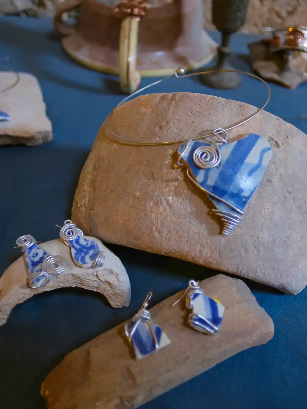 Handgefertigter, mit Draht umwickelter blauer und weißer Keramikschmuck, der auf Steinstücken ausgestellt ist.