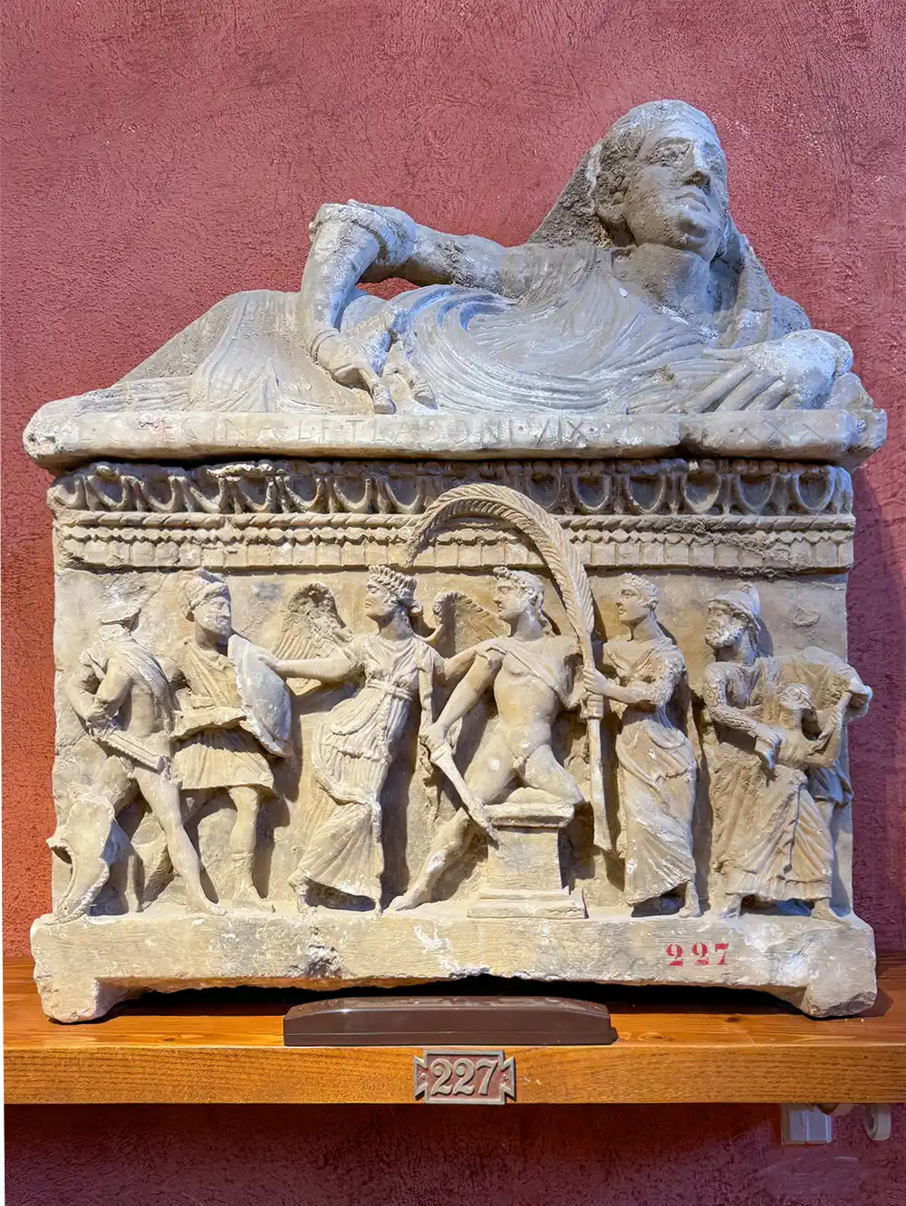 Antiker Steinsarkophag mit einer liegenden etruskischen Frauenfigur und geschnitzten Reliefs auf der Vorderseite.