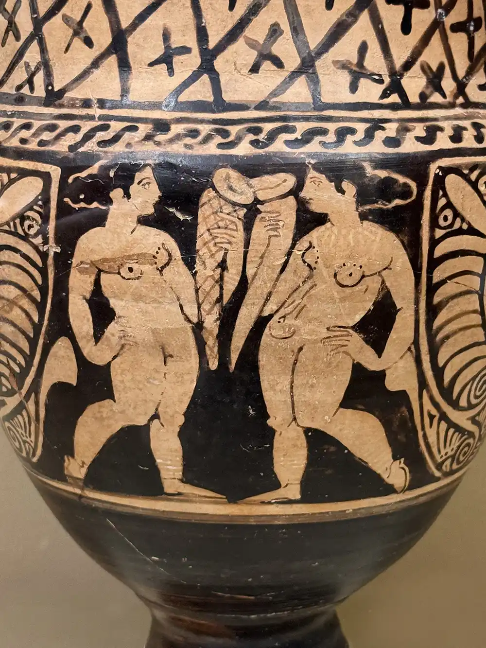 Antike griechische Vase mit zwei nackten Frauen, die neben zwei geflügelten Stäben mit ineinander verschlungenen Schlangen stehen.