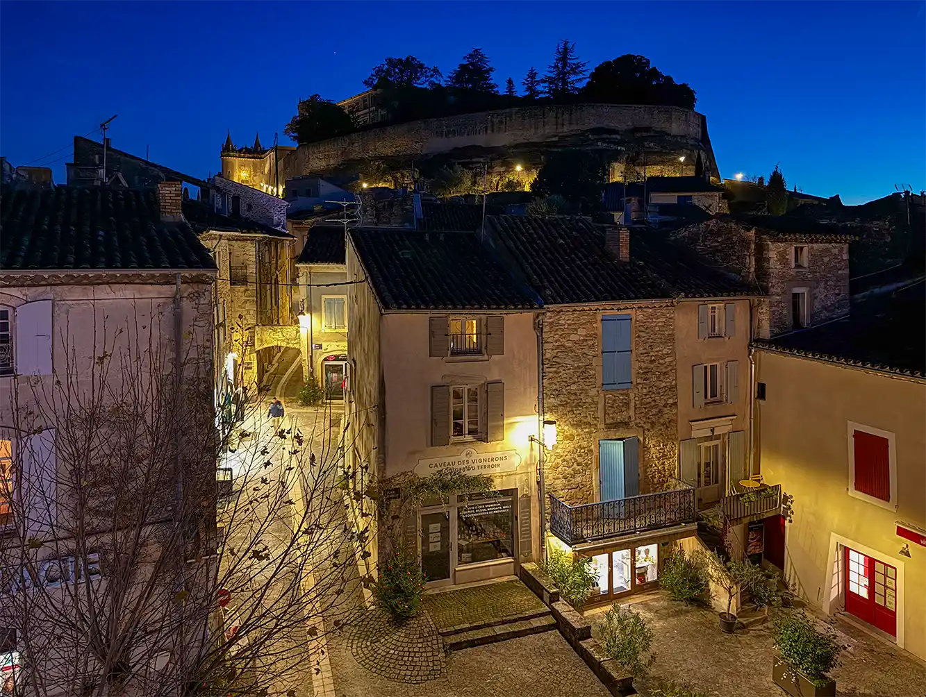 Grignan-Schloss-Abend Ein charmantes provenzalisches Dorf mit beleuchteten Kopfsteinpflasterstraßen und einer Burg auf einem Hügel in der Abenddämmerung.