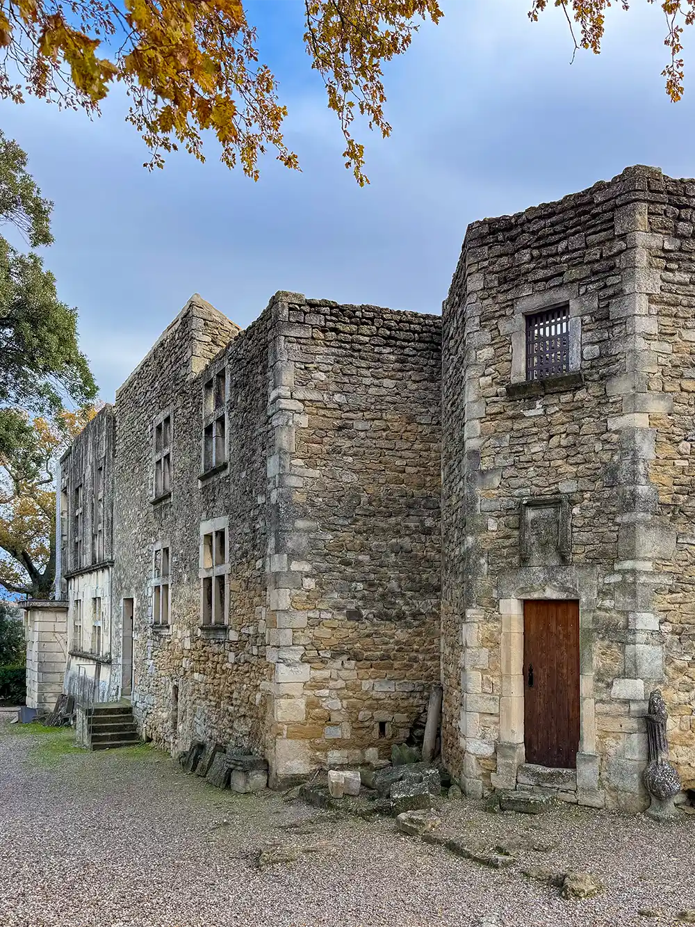 Grignan-Schloss-Ruinen Alte Mauern ohne Dach, mit Holztür und vergittertem Fenster, umgeben von Kies und Bäumen.