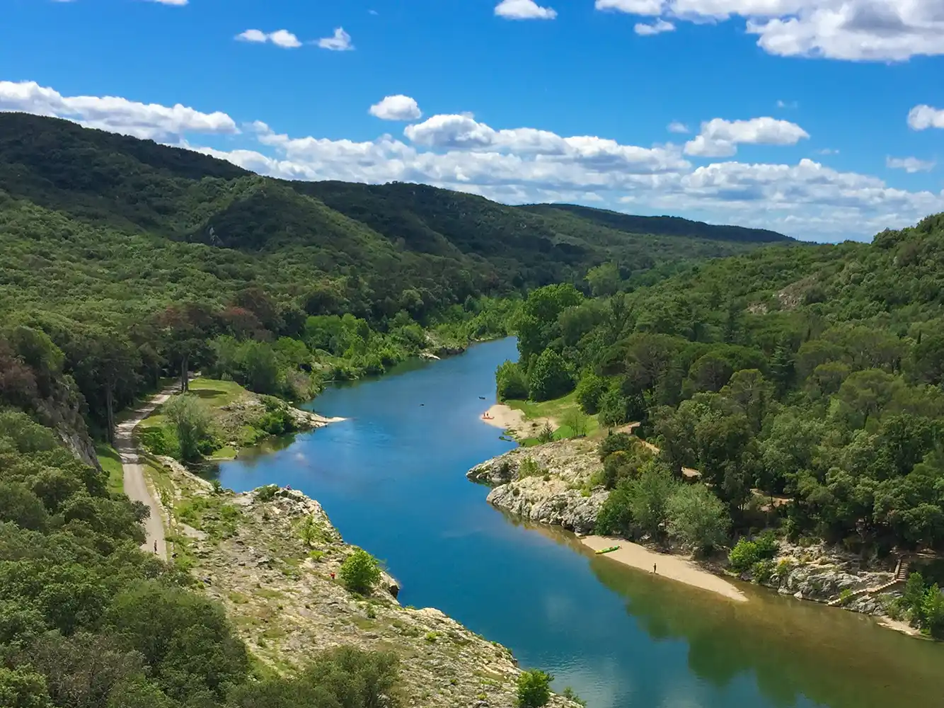 Ein gewundener Fluss fließt durch üppig grüne Hügel unter einem blauen Himmel mit vereinzelten weißen Wolken.