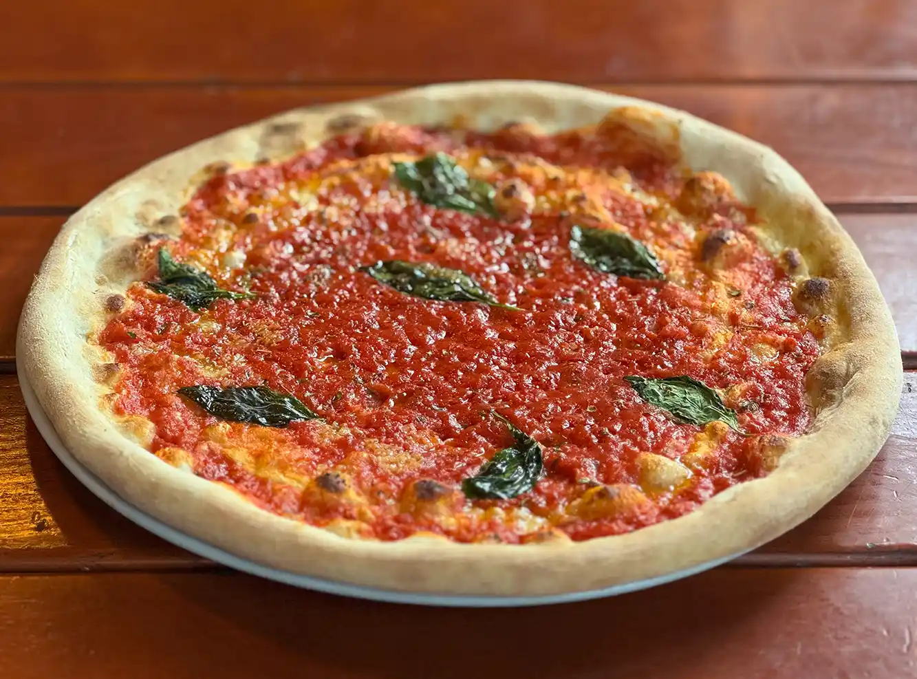 Eine ganze Pizza Margherita mit Tomatensauce, Käse und Basilikumblättern auf einem Holztisch.