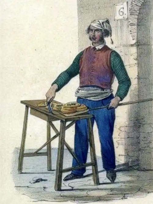 Eine Person in historischer Kleidung steht an einem Tisch und schneidet mit einem Messer rundes Gebäck auf.