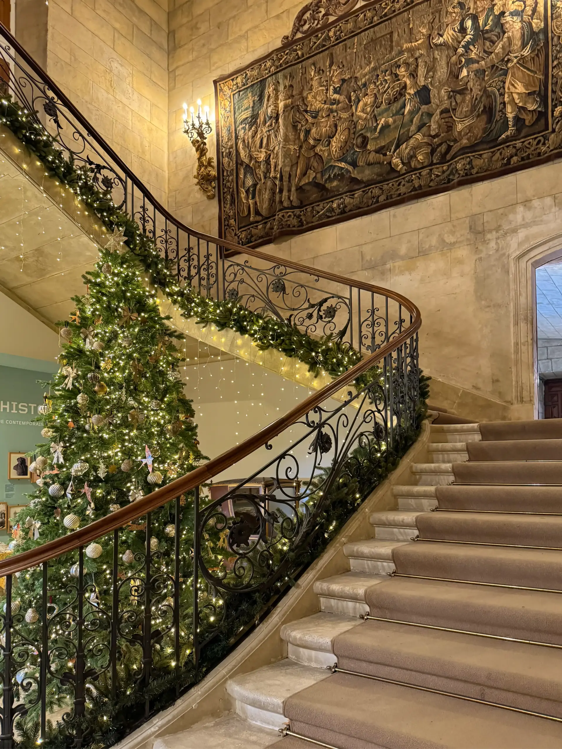 Schloss-Grignan-Eingangstreppe Große, mit Girlanden und Lichtern geschmückte Treppe, daneben ein großer Weihnachtsbaum in einer geschmückten Halle.