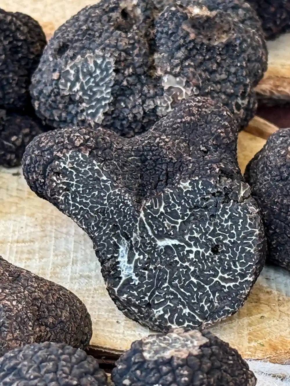 Trueffelmarkt-Richerenches-Perigord-Trueffel Nahaufnahme von schwarzen Trüffeln mit rauer, strukturierter Haut und weißer Maserung auf einer Holzoberfläche.