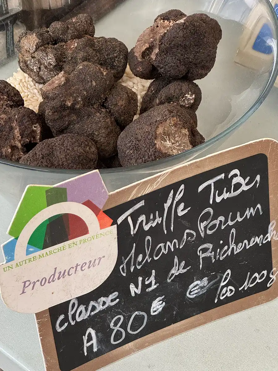 Trueffelmarkt-Richerenches-Trueffelpreis Eine Schale mit schwarzen Trüffeln, die zum Verkauf angeboten wird, mit einem Kreideschild mit Preisangaben.